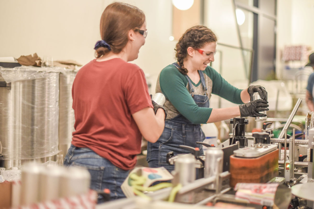 women adding labels to cans in brewery 1200x628 1